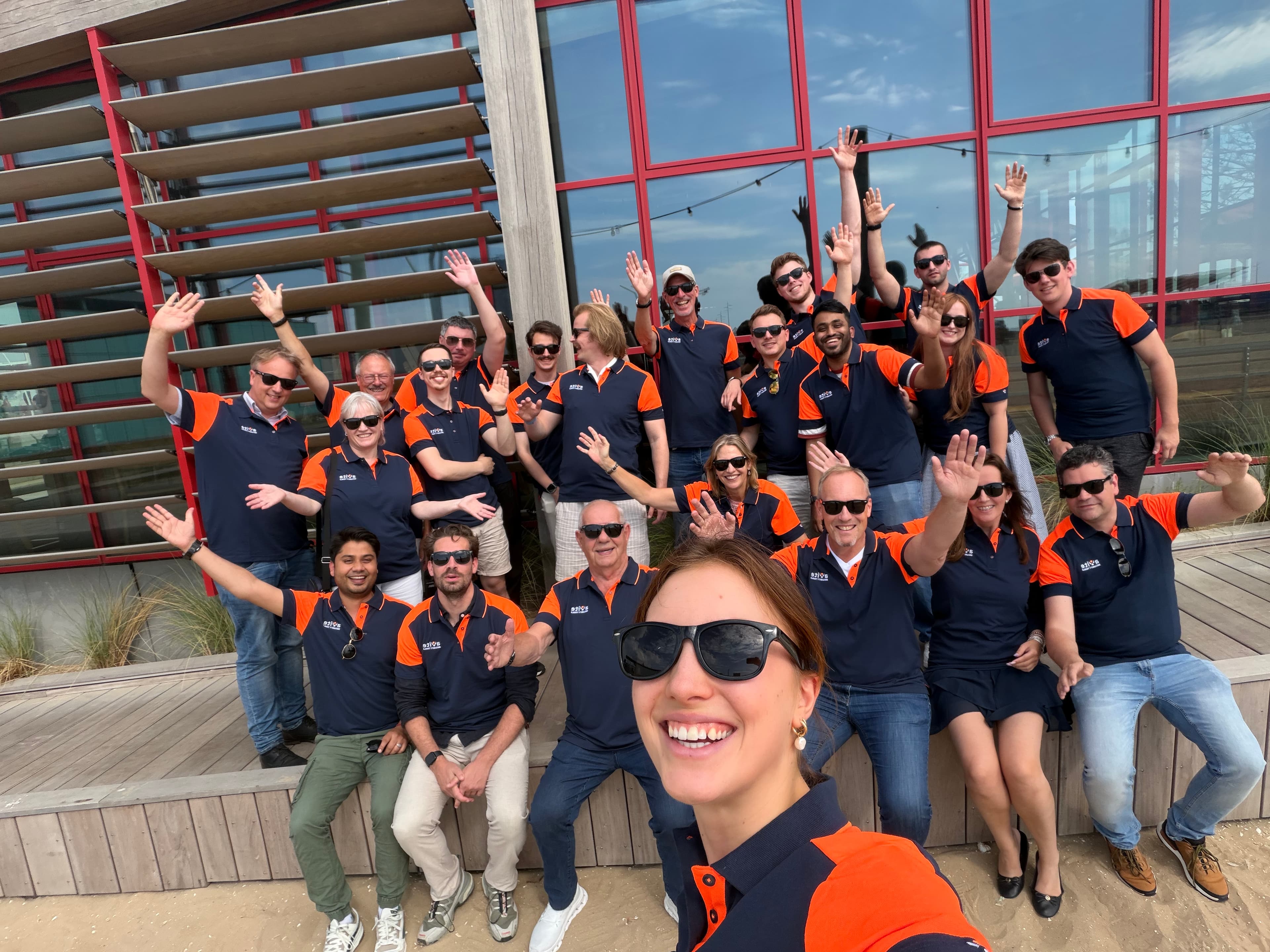 The aXite team gathered outdoors, smiling and waving at the camera.